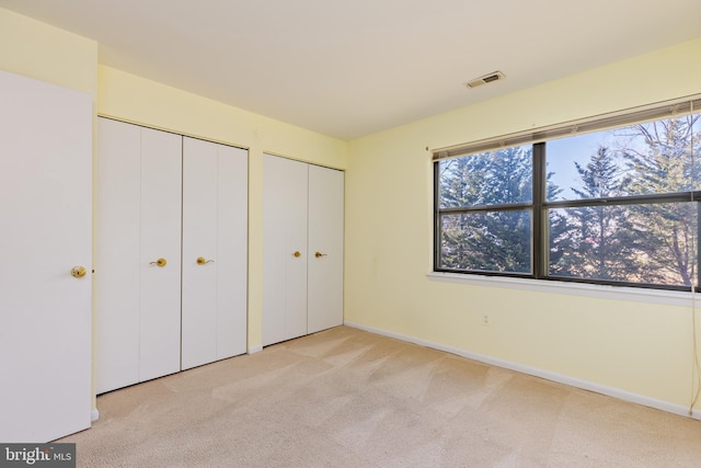 unfurnished bedroom with multiple closets and light colored carpet