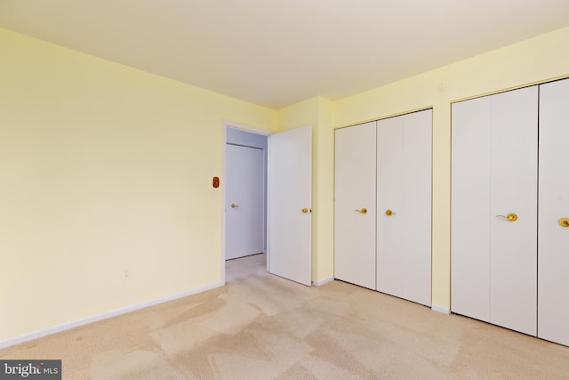 unfurnished bedroom featuring multiple closets and light carpet