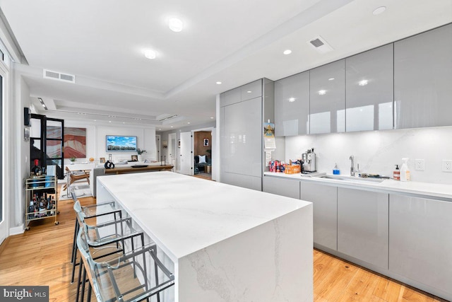 kitchen with a tray ceiling, a kitchen breakfast bar, sink, and light wood-type flooring