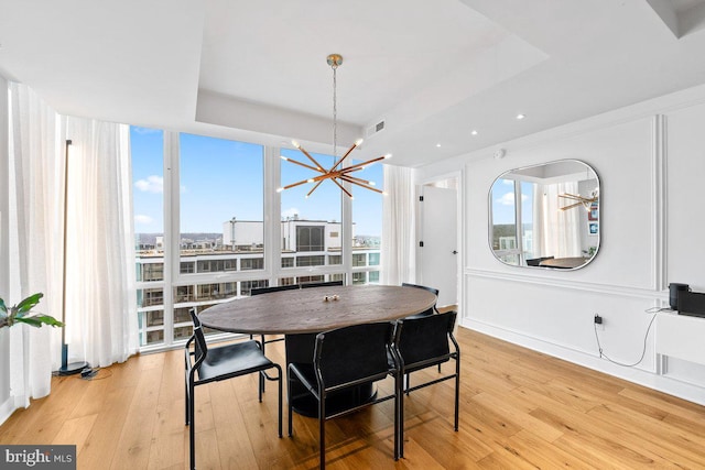 dining room with floor to ceiling windows, a chandelier, light wood-type flooring, and a tray ceiling