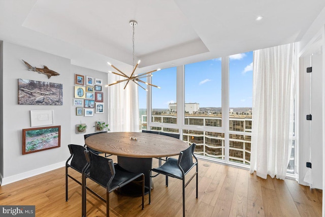 dining room featuring a chandelier, light hardwood / wood-style flooring, expansive windows, and a raised ceiling