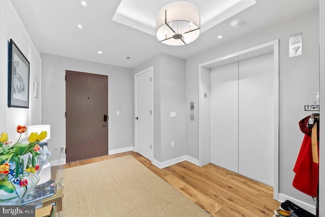 entryway with hardwood / wood-style flooring, elevator, and a tray ceiling