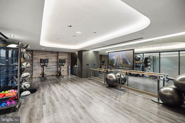 gym featuring hardwood / wood-style floors, a raised ceiling, and wood walls