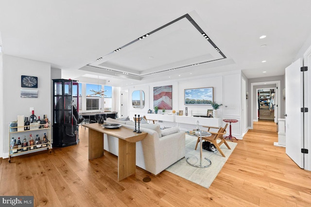 living room featuring a wealth of natural light, a raised ceiling, and light wood-type flooring