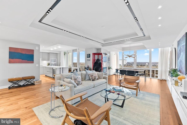 living room with expansive windows, a tray ceiling, and light wood-type flooring