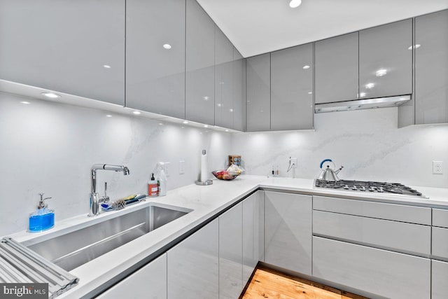 kitchen with stainless steel gas stovetop, sink, gray cabinetry, decorative backsplash, and light hardwood / wood-style flooring