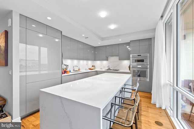 kitchen with a breakfast bar area, gray cabinetry, light hardwood / wood-style flooring, a kitchen island, and stainless steel double oven