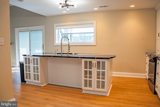 kitchen featuring stainless steel electric stove, dark countertops, visible vents, white cabinets, and a sink