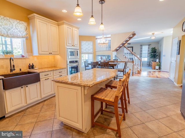 kitchen with sink, appliances with stainless steel finishes, light stone counters, a kitchen island, and decorative light fixtures