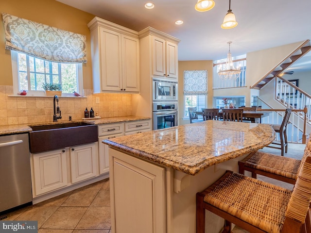 kitchen with hanging light fixtures, light stone countertops, appliances with stainless steel finishes, and sink