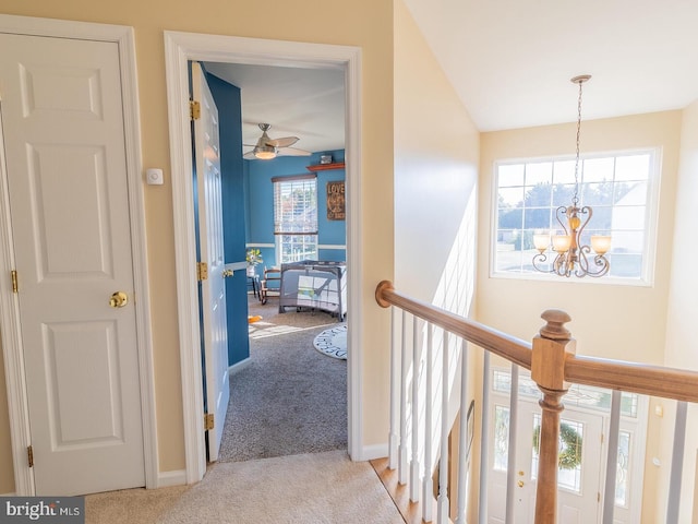 hallway featuring an inviting chandelier, light colored carpet, and a healthy amount of sunlight