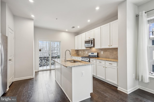 kitchen featuring appliances with stainless steel finishes, an island with sink, sink, white cabinets, and light stone countertops