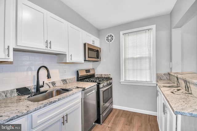 kitchen with appliances with stainless steel finishes, tasteful backsplash, sink, white cabinets, and light hardwood / wood-style flooring