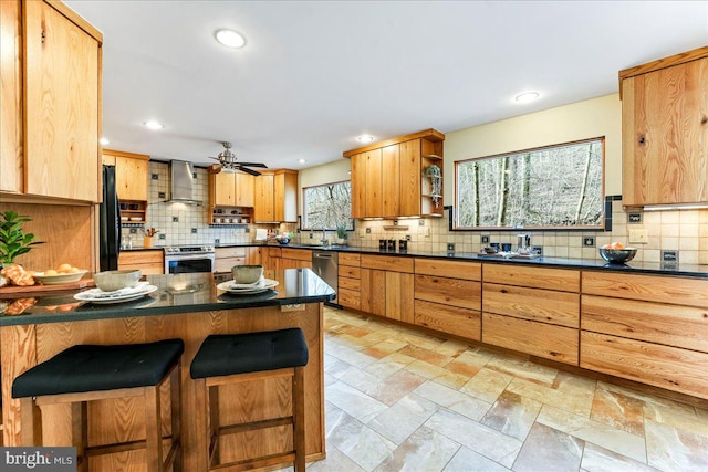 kitchen with dark countertops, wall chimney exhaust hood, a breakfast bar, stainless steel appliances, and open shelves