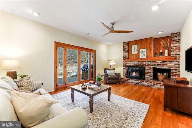 living room featuring light wood-type flooring, a brick fireplace, ceiling fan, and recessed lighting