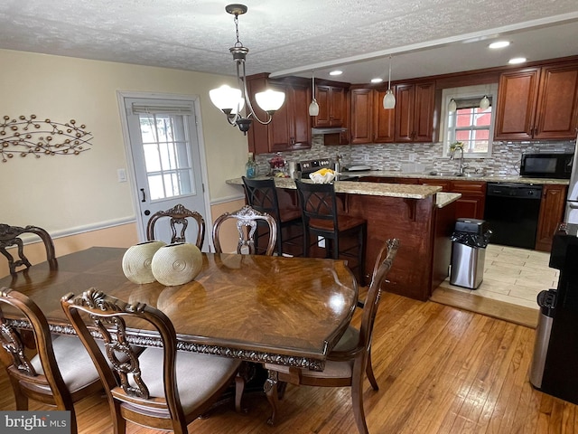 dining room featuring sink, a textured ceiling, a chandelier, and light hardwood / wood-style flooring