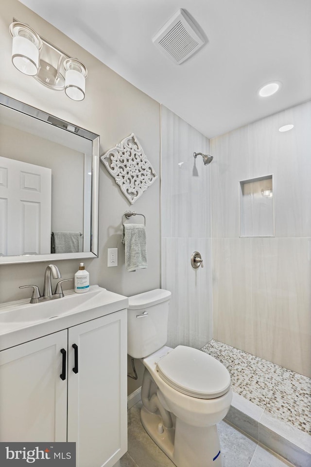 bathroom with tile patterned floors, toilet, a tile shower, and vanity