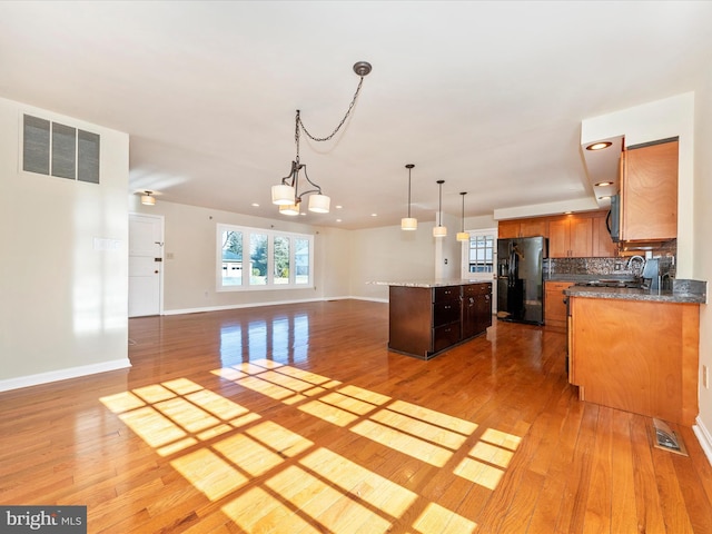 kitchen featuring light hardwood / wood-style floors, black appliances, decorative backsplash, a kitchen island, and decorative light fixtures