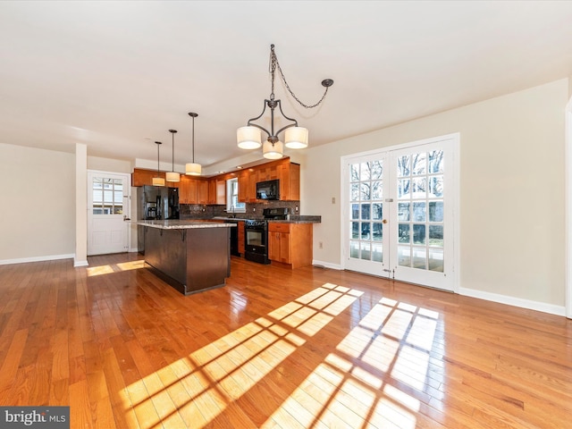 kitchen with a kitchen bar, black appliances, a kitchen island, pendant lighting, and backsplash