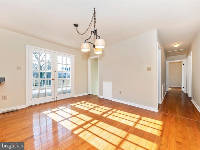 unfurnished dining area with an inviting chandelier, wood-type flooring, and french doors