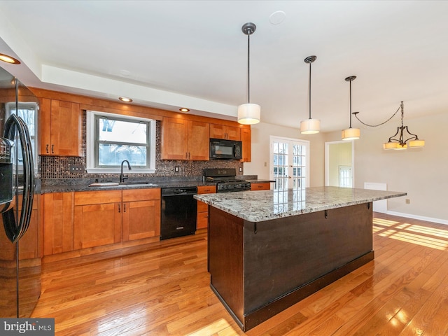 kitchen with sink, hanging light fixtures, a center island, light stone counters, and black appliances