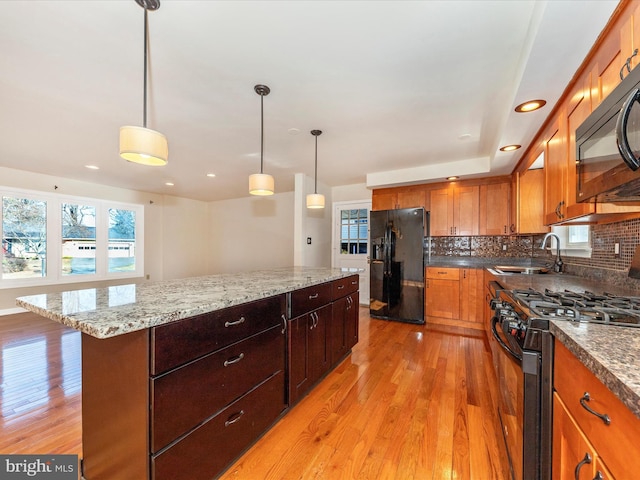 kitchen featuring light hardwood / wood-style flooring, a kitchen island, pendant lighting, decorative backsplash, and black appliances