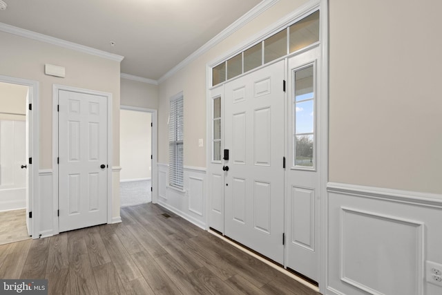 foyer entrance with a wainscoted wall, crown molding, and wood finished floors