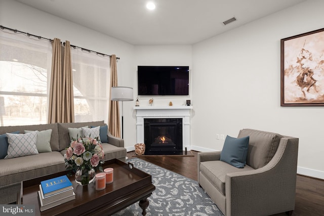 living room with baseboards, a lit fireplace, visible vents, and wood finished floors