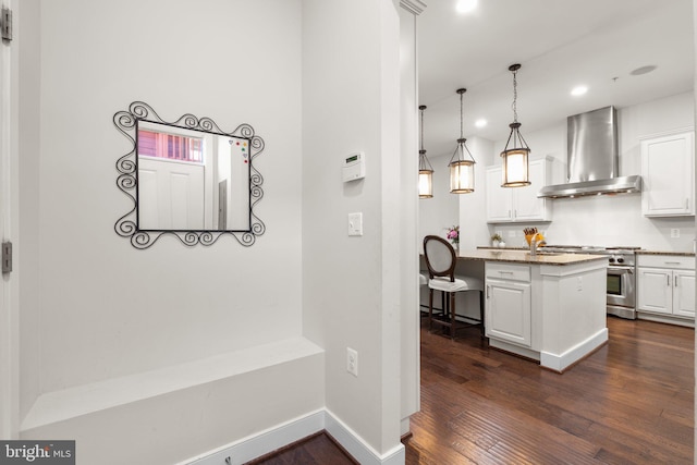 kitchen featuring dark wood-style floors, white cabinetry, wall chimney range hood, high end range, and a kitchen bar