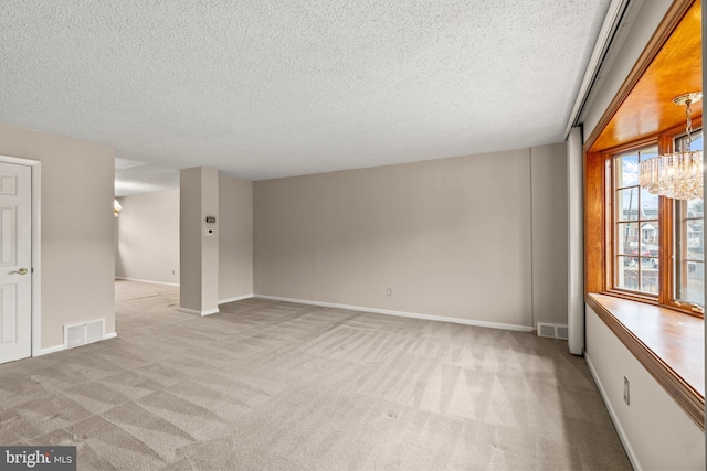 empty room featuring light colored carpet, a chandelier, and a textured ceiling