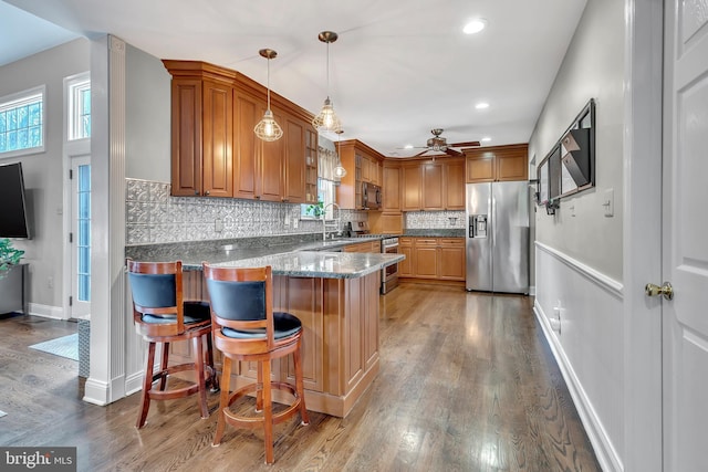 kitchen with brown cabinetry, a breakfast bar area, a peninsula, hanging light fixtures, and stainless steel appliances