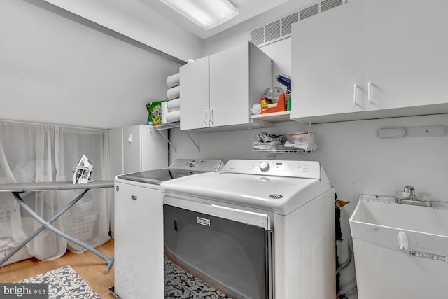 laundry room with washing machine and dryer, cabinet space, a sink, and light wood finished floors