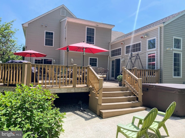 back of property with a wooden deck, a patio area, and a hot tub