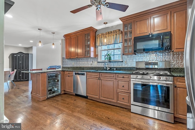 kitchen with decorative light fixtures, beverage cooler, a sink, appliances with stainless steel finishes, and glass insert cabinets