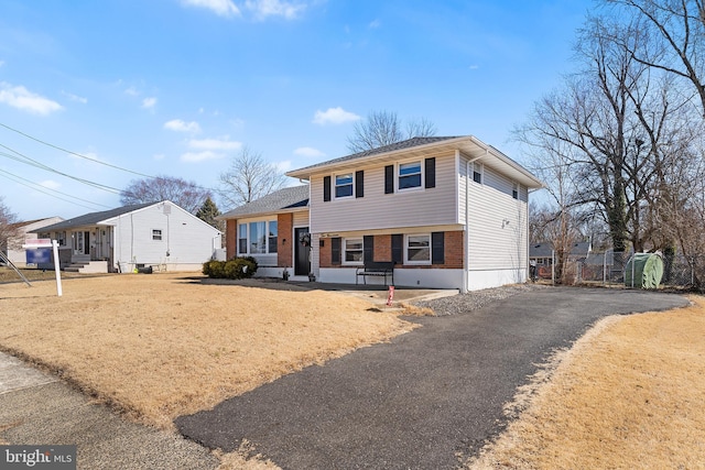 split level home featuring aphalt driveway, brick siding, and fence