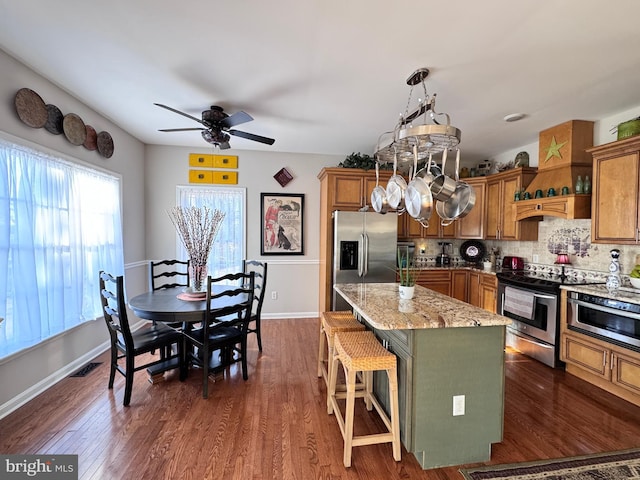 kitchen with light stone counters, a breakfast bar area, stainless steel appliances, hanging light fixtures, and a kitchen island