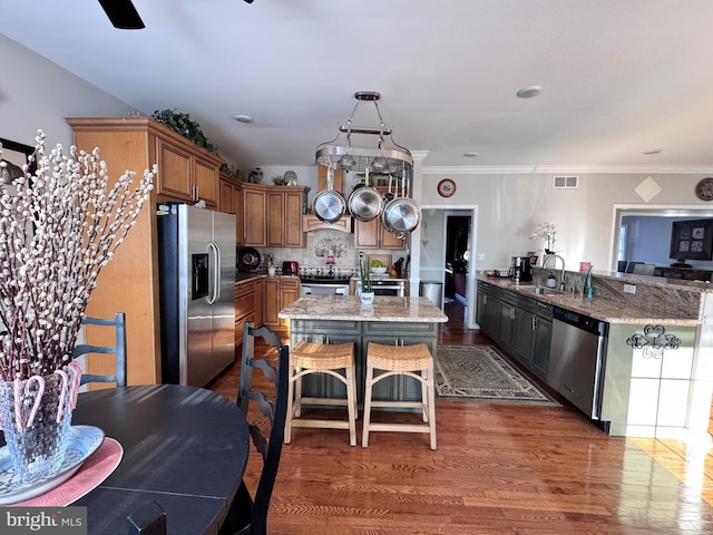 kitchen featuring light stone countertops, stainless steel appliances, a sink, brown cabinets, and dark wood-style floors