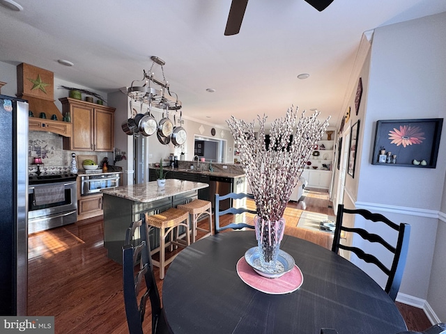 dining space featuring baseboards, dark wood finished floors, crown molding, and ceiling fan with notable chandelier