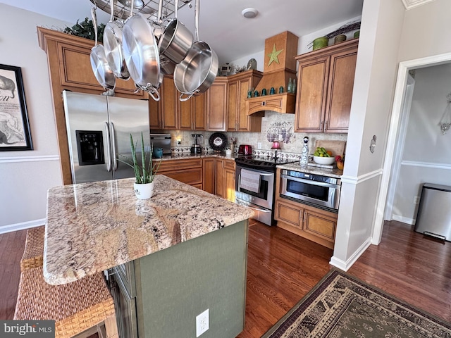 kitchen with light stone counters, appliances with stainless steel finishes, decorative backsplash, dark wood-style floors, and a kitchen bar