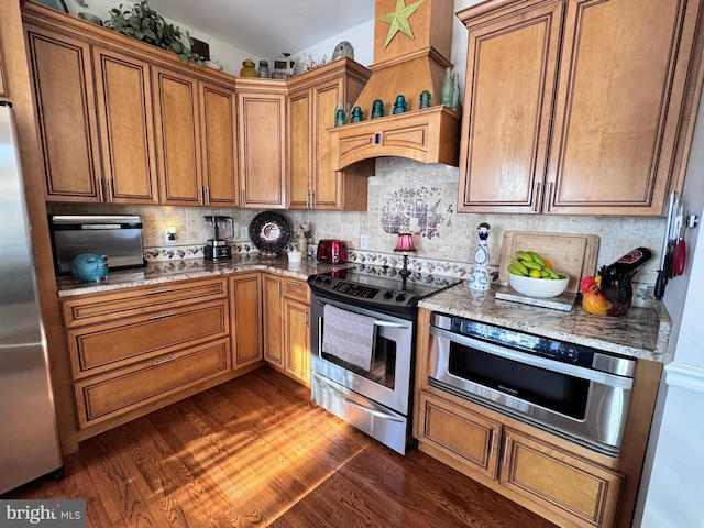 kitchen featuring stainless steel appliances, dark wood-type flooring, light stone counters, and decorative backsplash