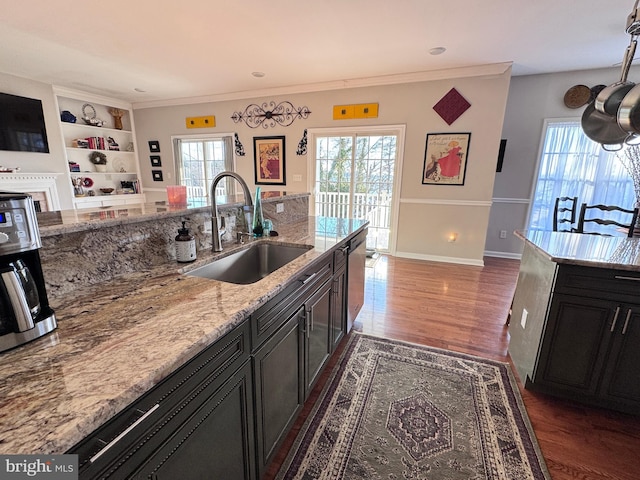 kitchen featuring light stone counters, dark wood-style floors, crown molding, a sink, and baseboards