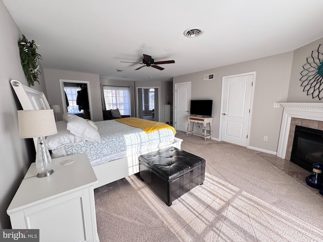 carpeted bedroom featuring ceiling fan, a tile fireplace, visible vents, and baseboards