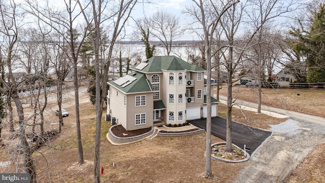 view of front facade with a garage, solar panels, a water view, driveway, and roof with shingles