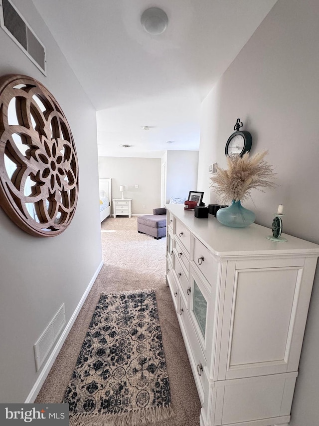 hallway featuring dark colored carpet, visible vents, and baseboards