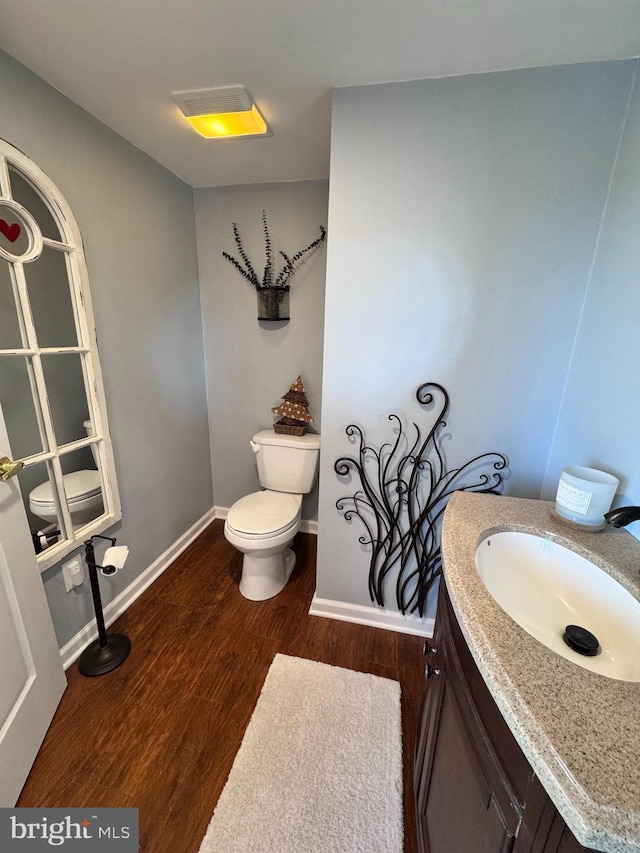 bathroom featuring toilet, baseboards, wood finished floors, and vanity