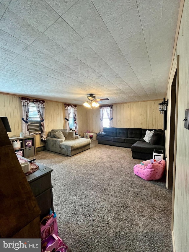 carpeted living room featuring ceiling fan, wooden walls, and a textured ceiling