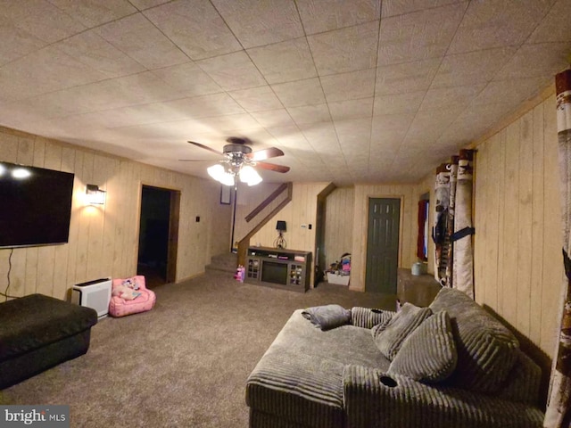 carpeted living room with ceiling fan and wood walls