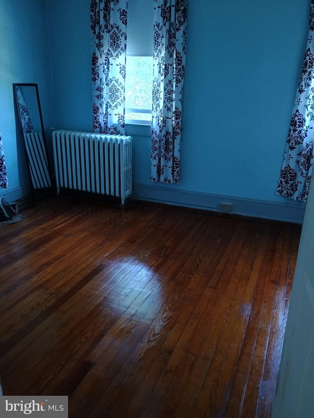 spare room featuring radiator heating unit and dark hardwood / wood-style floors