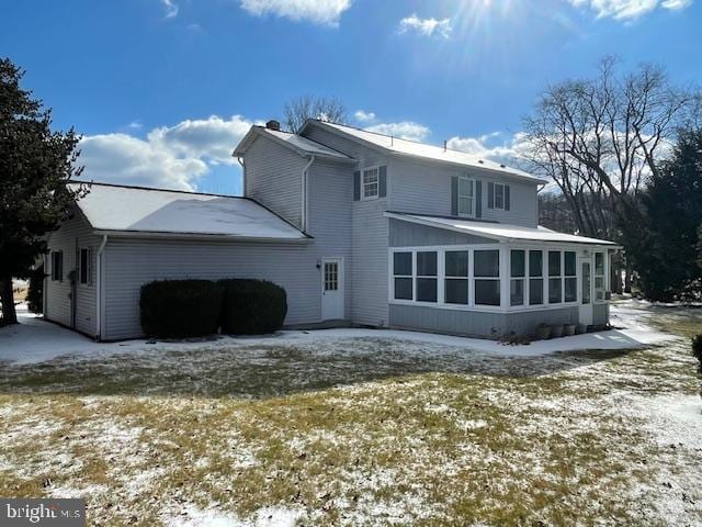 snow covered back of property with a sunroom