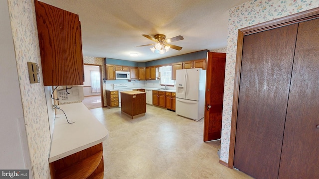 kitchen with sink, white appliances, a textured ceiling, a kitchen island, and ceiling fan